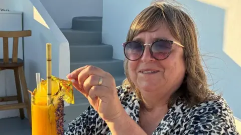 Imagen proporcionada: Una mujer con gafas de sol y una camisa con estampado de leopardo sostiene un cóctel amarillo. Sonríe y mira a la cámara.