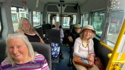 Jane Bishop Five elderly people in a minibus, looking at the camera and smiling