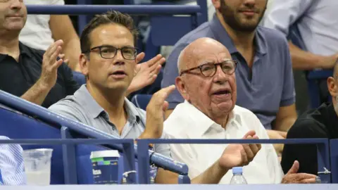 Getty Images 拉克蘭·默多克 (Lachlan Murdoch) 和他的父親魯珀特·默多克 (Rupert Murdoch) 在 2018 年美國網球公開賽上合影，他們在看台上鼓掌。兩人似乎都在觀看比賽