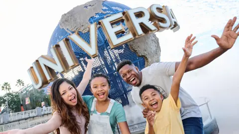 A large blue globe on display outside a Universal theme park in the USA, with four people outside with their mouths open, and arms outstretched.