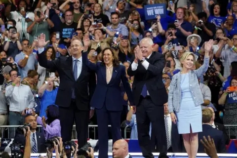 Reuters Doug Emhoff, Kamala Harris, Tim Walz and Gwen Walz wave at a crowd