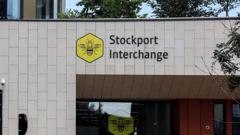 BBC An exterior shot of Stockport Interchange. It is a grey-panelled building and has the yellow bee network logo on the front.