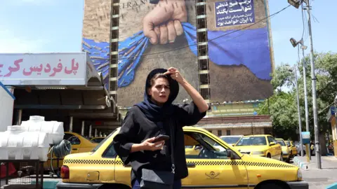 An Iranian woman walks near a huge billboard referring to the Strait of Hormuz and words reading in Persian 'Forever in Iran's hand' at Vanak square in Tehran, Iran, 06 May 2026.