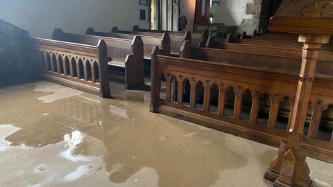 Water in the ground in front of the pews