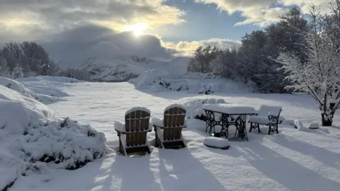 BBC Weather Watchers/Janey G Snow covered outdoor furniture, seen the from back, looking out towards snow-covered mountains. 