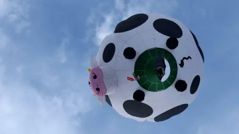 Reuters The underneath of a cow-shaped hot air balloon flying in the sky.