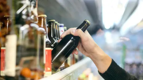 Getty Images A hand lifting a beer bottle off a supermarket shelf.