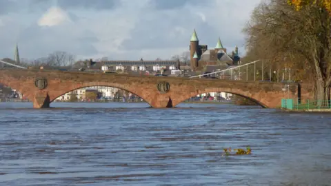Getty Images A river in spate flows underneath the arches of a sandstone bridge with the town of Dumfries in the background