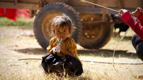 A child kneels down with a juice carton in a refugee camp in Cambodia