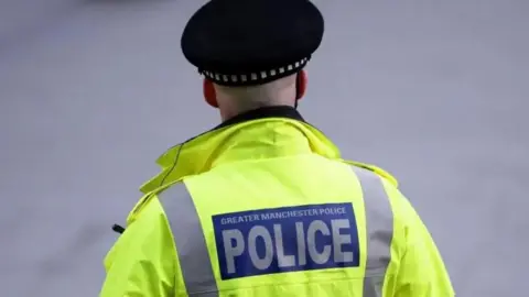 Greater Manchester Police officer taken from behind wearing a hi-vis jacket and police hat