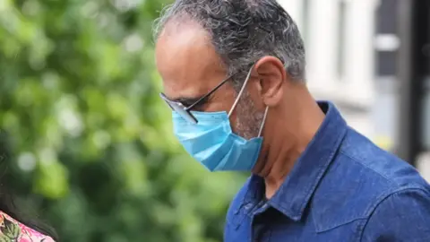 A man wearing glasses, a blue face mask and a blue shirt.