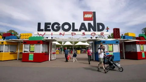 Getty Images The entrance to LEGOLAND with a huge sign bearing the theme parks name, ticket kiosks, and large Lego bricks of various colours. Some families can be seen making their way out of the park. 