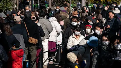 Getty Images Thousands of people wait in line to take a last look at twin giant pandas Xiao Xiao and Lei Lei on their final public viewing day at Ueno Zoological Gardens in Tokyo on 25 January. The visitors are clad in winter wear and many also have masks on.