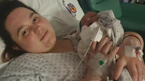 Family photo Heather lying on a hospital bed in hospital gowns just after giving birth pictured holding her daughter. 