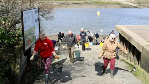 Michelle Collier Several volunteers carrying buckets up a concrete slope, they're walking towards the camera