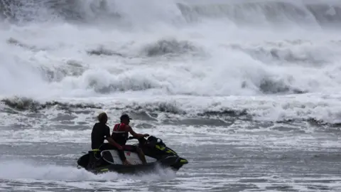 A jet ski with a surfer in large waves