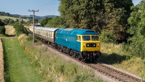 Steve Tucker A bright blue and yellow old fashioned train in a shed.