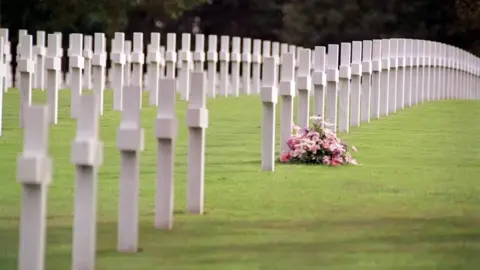 Martin Walter/PA Media A pink floral wreath sitting among white crosses