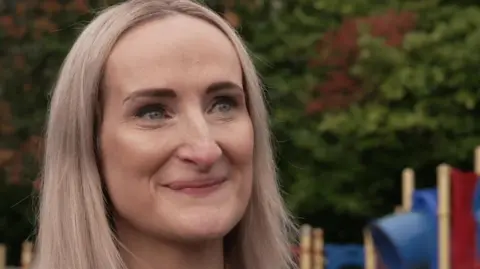 Esther Whitaker has long blonde hair and is stood in a children's playground