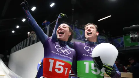 Team GB's Tabitha Stoecker and Matt Weston acknowledge fans after winning gold in the skeleton mixed team event at Cortina Sliding Centre