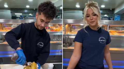 Mitch Key pouring vinegar onto some fish and chips while Destiny Harold is behind the counter of a chip shop. 