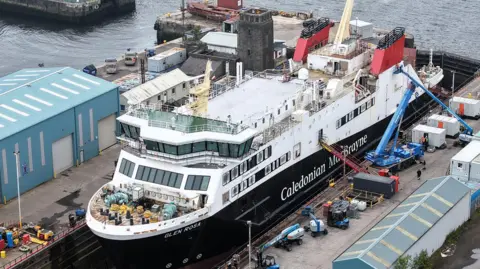 A large black and white ship with red funnels in a dry dock