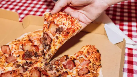A file image of a pizza being picked up out of a box by a hand