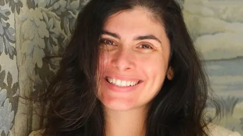 A woman with dark hair looks at the camera, smiling