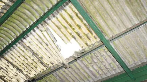 Health and Safety Executive A close up of the dirty, fragile corrugated plastic panel, that the worker fell through. A shaft of light shines through the hole in the panel.