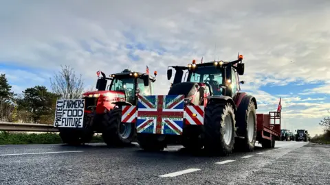 BBC/Linsey Smith Two tractors side by side on a road. One vehicle has a placard on the front which reads: Protect farmer's food future. The other has a Union flag with writing on it.