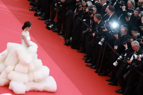 EPA An actress in an elaborate voluminous white dress on the Cannes red carpet facing a bank of photographers in black tie.