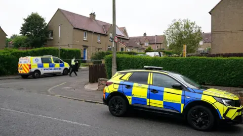 a police car and police van parked in the street outside a cordoned-off house