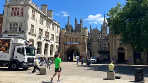 Shariqua Ahmed/BBC Cathedral Square, with the Cathedral in the background, with some people walking around in the square.