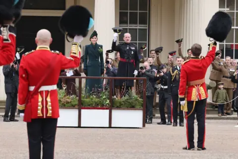 Getty Images Princess of Wales standng on a podium while several soldiers in uniform hold their hats and caps in the air.