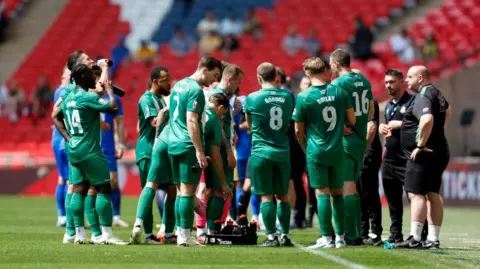 PA Media Wakering players in green strip gather on the pitch