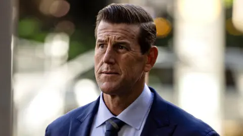 Sam Mooy / The Sydney Morning Herald via Getty Images A front-on shot of Roberts-Smith looking pensively away from camera while wearing a suit and tie with strong background bokeh, as he walks along a street while arriving at the Federal Court in Sydney in May 2025.