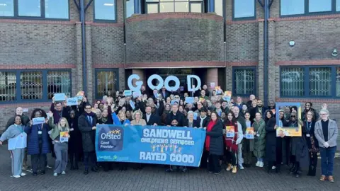 A large group of people with a blue flag standing outside a brown brick building