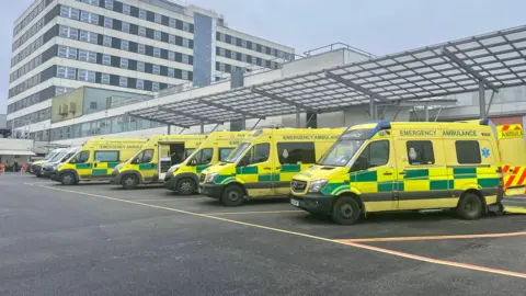 A row of ambulances are parked outside a hospital