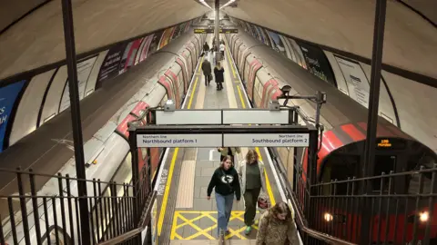 BBC Platform at Clapham Common station shows two Tube trains and passengers walking along it