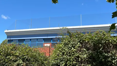 A building on Hopton Industrial Estate in Devizes with netting on its roof and green bushes in the foreground and a blue sky in the background.
