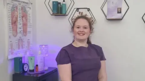 Liz at the ZenDen Woman in front of massage paraphernalia