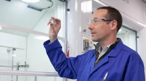John Griffin/Lancaster University John Griffin, wearing a blue lab coat and safety specs, looks at a glass slide.