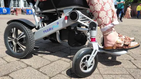 A picture of the lower part of a grey and black wheelchair with someone sitting in it.