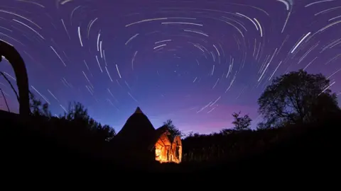 A time-lapse image of a farm in darkness under a purple star-filled night sky