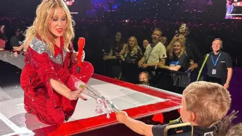 Kylie Minogue on stage in Birmingham being handed a pink rose by three-year-old fan Reuben