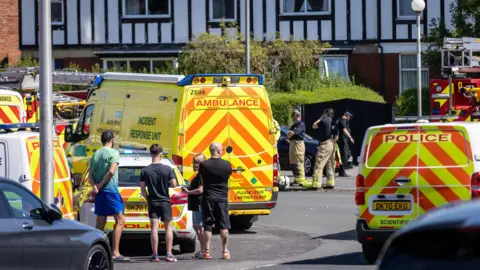 PA Media Locals watch as ambulances and police block the road 