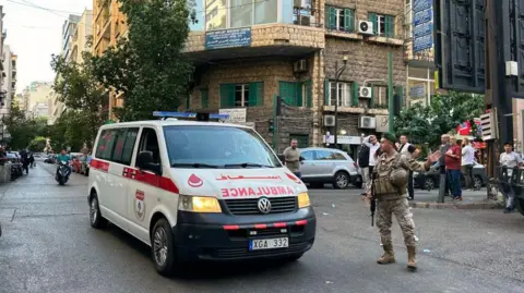 Getty Images Sebuah ambulans melaju melewati seorang tentara di Lebanon setelah serangan