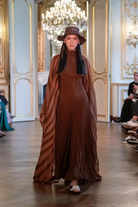 Rooful Ali A model wearing a long brown dress combined with a bucket hat