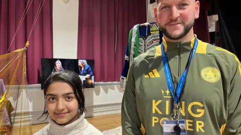 14 year old Marina stands next to Joe who's wearing a Leicester City Shirt.
behind is an exhibition in fearon hall. 
