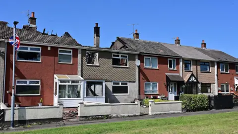 A row of terraced houses, two showing fire damage with roofs partially missing